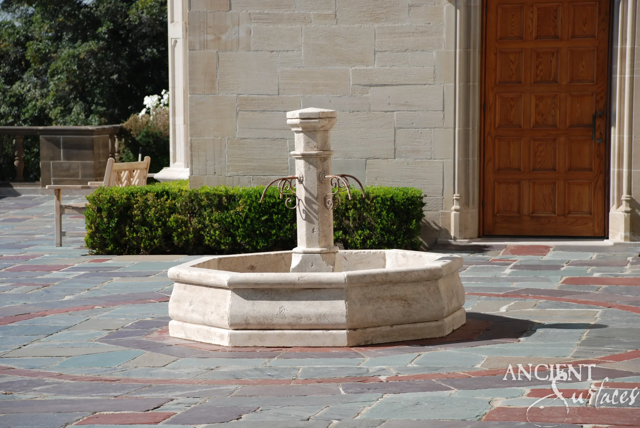 Reclaimed limestone garden fountain installed on a colored-stone patio beside a carved limestone facade