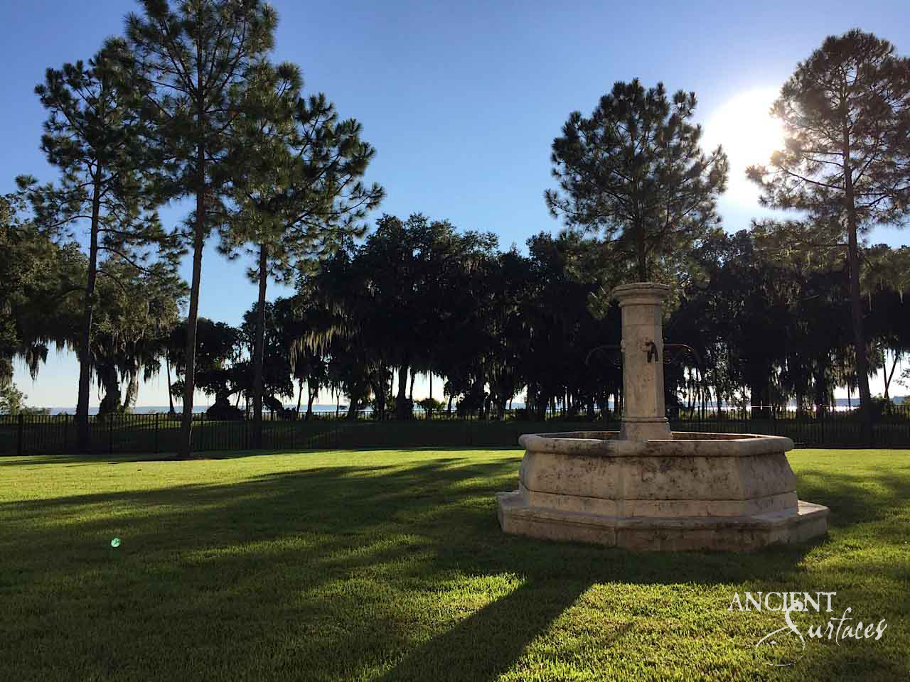 Reclaimed limestone garden fountain on a sunlit lawn framed by pines at golden hour